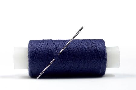 Close-up of spool of blue sewing thread with steel needle over white background