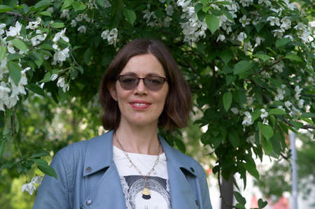 Closeup portrait of positive brunette girl on spring sunny street . She wears sunglasses and blue...