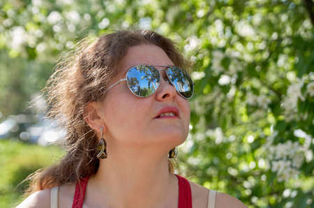 A woman in a red singlet and mirrored sunglasses stands in front of a woodpileの写真素材