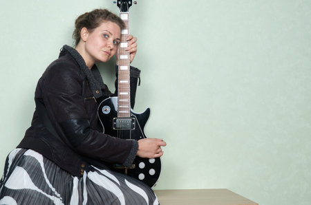 Woman with curly hair in leather jacket playing black electric guitarの写真素材
