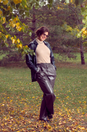 A woman in leather clothes stands in an autumn parkの写真素材