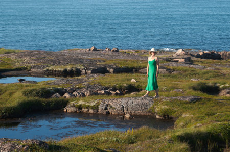 Woman tourist in a straw hat and a green dress on the seashore on a bright sunny dayの写真素材