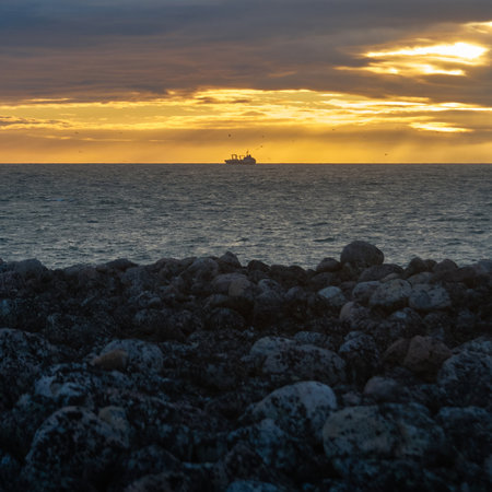 Silhouette of a fishing ship on the horizon of the sea against the backdrop of a dramatic sunset with sunbeamsの写真素材