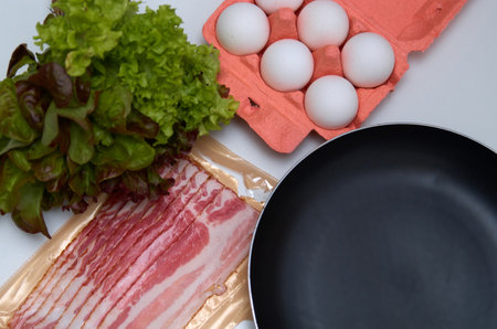 Cooking scrambled eggs with bacon: eggs, bacon, lettuce and a frying pan on the kitchen tableの写真素材