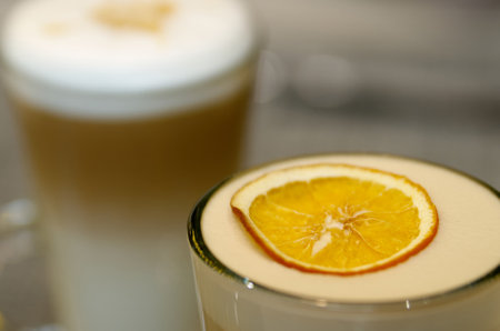 A slice of orange lies on the milk foam of a coffee drink in a glass cupの写真素材