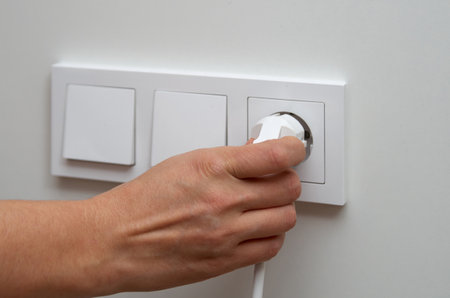 Woman's hand plugs an electric plug into a socket