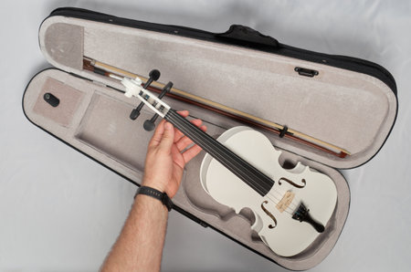 A man's hand takes a white violin out of its caseの写真素材