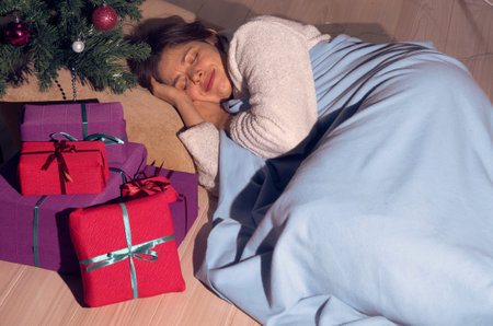 A woman in home clothes sleeps under a decorated Christmas treeの写真素材