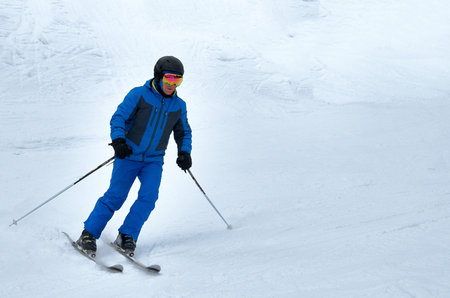 A man in blue sportswear on skis rides down a snowy slopeの写真素材