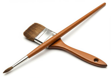 Two paint brushes are crossed on a white background. One is a round brush and one is a flat brush. Both have wooden handles and are used for painting and creating art. They are clean and ready for use.の素材