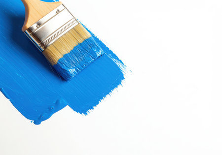 A paintbrush with blue paint is shown on a white surface. The brush has just made a stroke, leaving a vibrant blue mark. It suggests creativity, art, renovation, and the application of color to a surface.の素材