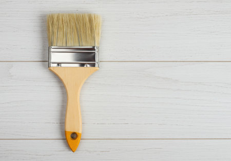 A paint brush with a yellow handle and natural bristles is displayed on a white wooden surface. The brush is clean and unused, suggesting readiness for painting or decorating projects. Top view.の素材