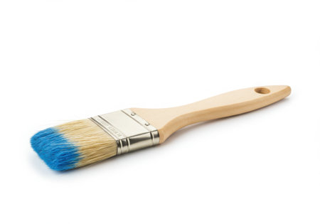 A paint brush with a wooden handle and blue paint on the bristles is isolated on a white background. The brush is angled, showcasing the bristles, metal ferrule, and the handle's shape, highlighting its use for painting.の素材