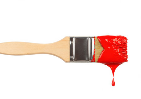 A paintbrush with a wooden handle is saturated with vibrant red paint. Droplets of paint hang from the bristles, showcasing the thick texture and rich color of the paint against a clean, white backdrop.の素材
