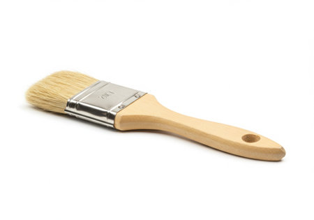 A paint brush with a wooden handle and light bristles is lying diagonally. The brush is clean and unused, set against a bright white background, highlighting its simple design and functionality.の素材