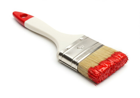 A paintbrush with a white handle and red accents, partially covered in red paint, lies diagonally on a white surface. The bristles are thick with paint, suggesting recent use for artistic or home improvement projects.の素材