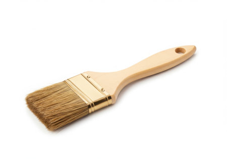 Isolated paint brush with a wooden handle and golden metal ferrule. The bristles are light brown. The tool is positioned diagonally on a white background, casting a subtle shadow. Useful for painting projects.の素材