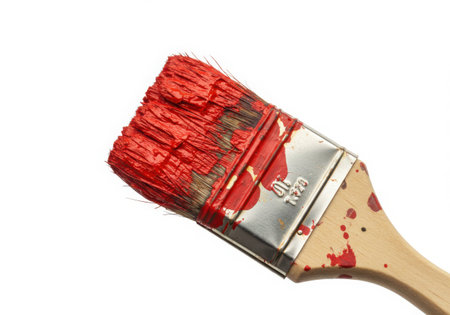 A close-up shot of a paintbrush covered in vibrant red paint. The wooden handle and bristles are visible, with splatters of paint adding texture. Isolated against a clean white background, highlighting the tool's use.の素材