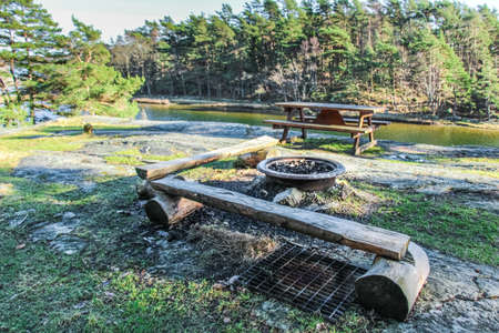 Wood bench, table and outdoor bbq in a swedish lake surrounded by rocks and forestの写真素材