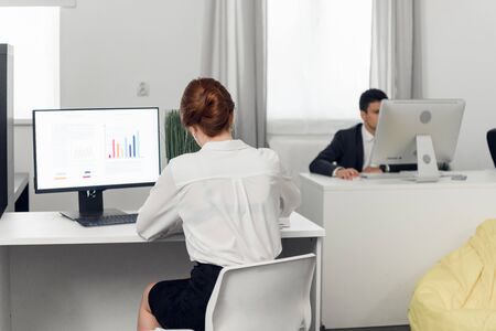 Man and woman in suits sit at tables and work with laptops in the office