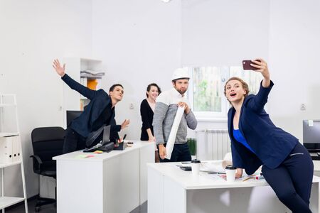 Young people having fun in the office, posing, making faces and taking selfies with a smartphone