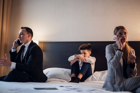 A modern business couple portrait - young man and woman on their phones, while noone is paying attention to their childの写真素材