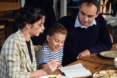 A girl doing her homework at the kitchen table with her parents being around