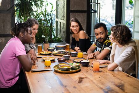 A multicultural group of young people in a cafe, eating asian food, drinking cocktails, chattingの写真素材