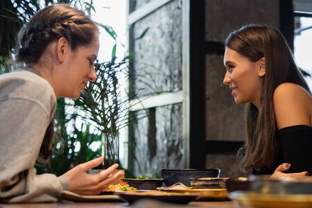 Two female friends chatting and having some snacks in a cafeの写真素材