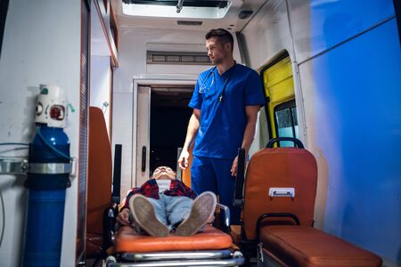 Unconscious woman lying on a stretcher in an ambulance car, a paramedic providing her first aid