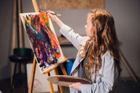 A little girl artist draws a picture with a brush in the Studio. A talented young schoolgirlの写真素材
