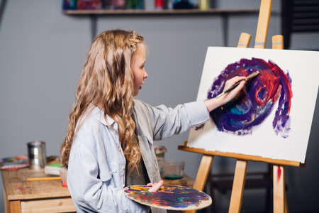 First lesson in art school, a little girl learns to draw and makes her first oil painting on canvas.の写真素材