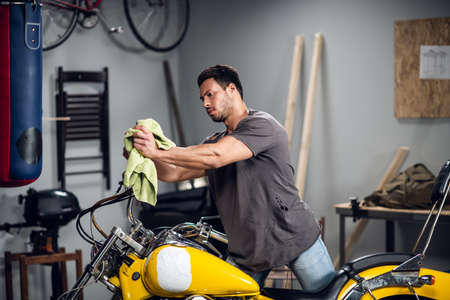 A strong male biker repairs his motorcycle in the garage. Interior of the workshop.の写真素材
