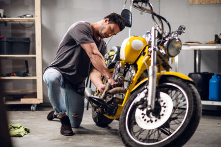 A young sports motorcycle repairman in a garage or workshop is working on a yellow bike.の写真素材