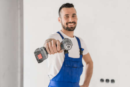 Cheerful builder points with a drill to the cameraの写真素材