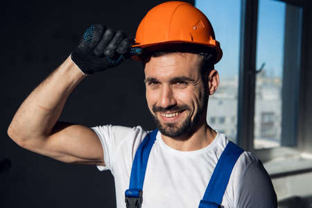 Handyman in overalls holds on to the visor of a hard hat