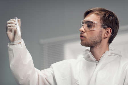 Closeup portrait of a man holding a test tube with white turbid liquid, research prosess in a medical laboratoryの写真素材
