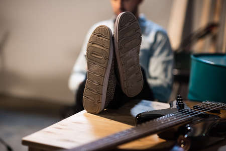 the guy is sitting with his feet in sneakers on the table, on the table is a bass guitar, close-up, a scene for product placement.の写真素材