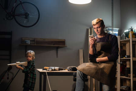a carpenter uses a break from work to place an order over the phone, a boy plays with a newly made...