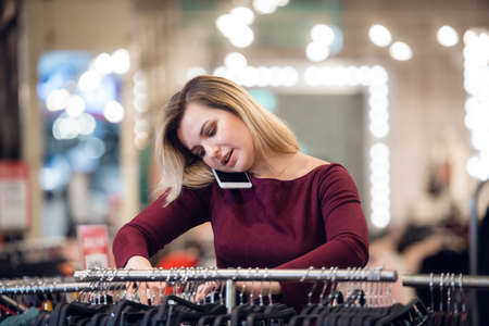 Smiling young woman talking on a mobile phone, while shopping in a retail store.の写真素材