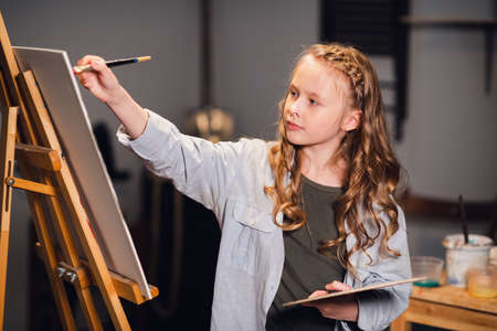 A little girl artist draws a picture with a brush in the Studio. A talented young schoolgirl.