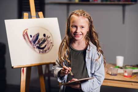 First lesson in art school, a little girl learns to draw and makes her first oil painting on canvasの写真素材