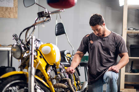 Private vehicle repair shop. Tuning a yellow chopper by a young mechanicの写真素材