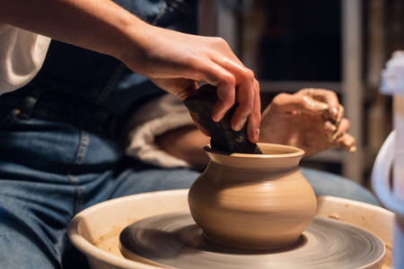 a Potter girl sculpts a pot on a Potters wheel with her hands and toolsの写真素材