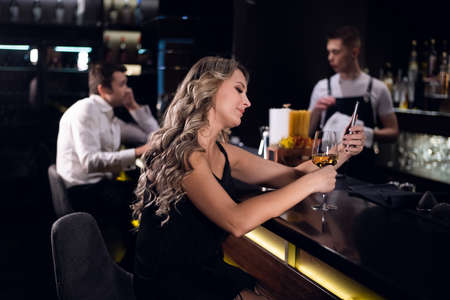 beautiful woman drinks white wine and surfs the Internet via smartphone in a cafe.の写真素材