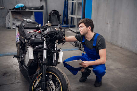Machinistin uniform writes on a clipboard and checks a motorcycleの写真素材