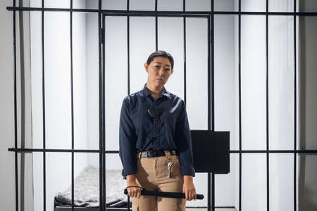 A young prison guard poses in front of prison bars in uniform. In a maximum security prison.