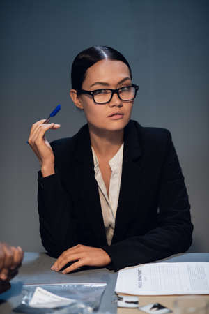The state prosecutor in a black business suit and glasses sits at a desk with documents holding a pen.の写真素材
