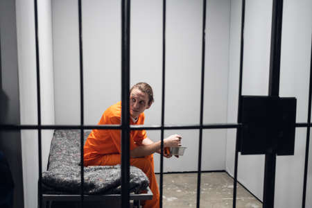 Dinner in a prison cell. A prisoner eats tasteless food from an iron bowl under guard behind bars