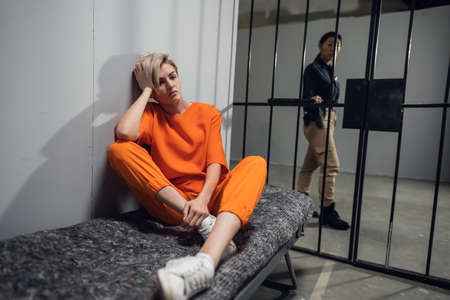A young pretty blonde prisoner in a general regime prison is sitting in a solitary cell.の写真素材